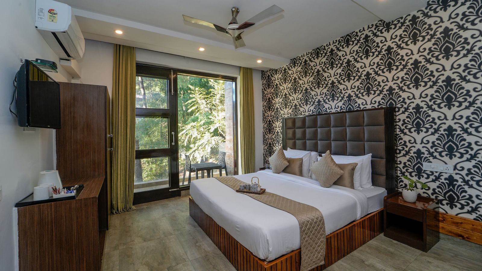 The deluxe room at DLS Whispering Winds featuring a bed, bed side tables, flat screen TV, other room amenities and a glass door leading to the balcony